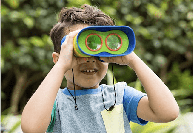 Niño explorando con binoculares al aire libre como ejemplo de juguetes educativos al aire libre