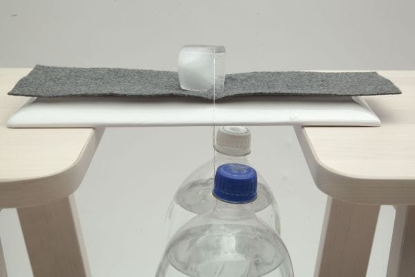 Un alambre que descansa sobre un cubo de hielo, sujetado por dos botellas pesadas.
