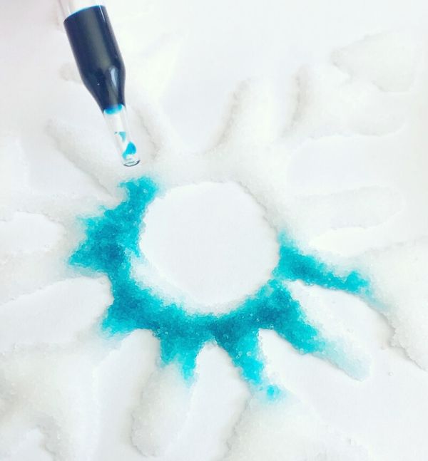 Se gotea líquido azul sobre una forma de copo de nieve hecha de sal