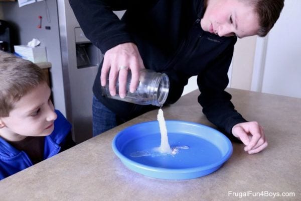 Un niño pequeño observa cómo un niño grande vierte "hielo caliente" de un frasco en un plato