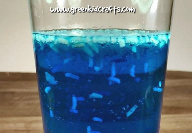 Una taza de líquido azul en el que el arroz flota y se mueve (ciencia preescolar)