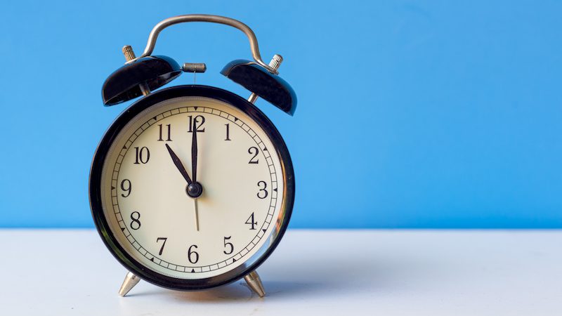 ¿Puede más de medio día ayudar con la escasez de maestros y el agotamiento? Despertador apuntando a las 11:00 en un escritorio blanco.