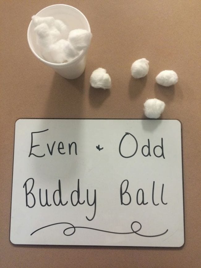 Lectura de pizarra Par + Odd Buddy Ball junto a una taza de bolas de algodón y cuatro bolas de algodón sueltas