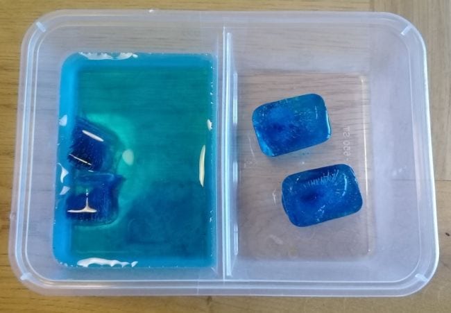 Cubos de hielo azul en un recipiente separado, también con agua a la izquierda (actividad de cambio climático)