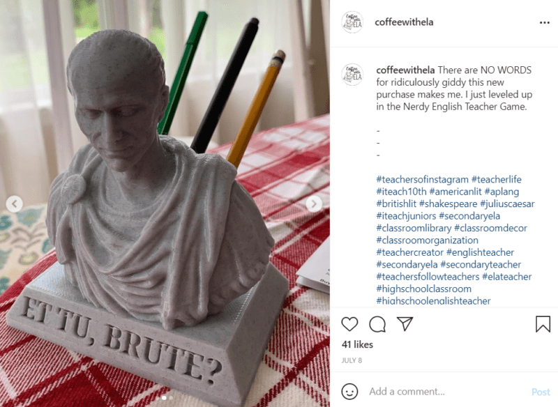 Un busto gris de Julio César se sienta sobre una mesa cubierta con un mantel de guinga.La frase "Et Tu, Brute?" En el busto, se pueden guardar lápices y bolígrafos en la parte posterior del busto para replicar la apariencia de un emperador romano apuñalado, como ejemplo de decoración de aula de secundaria