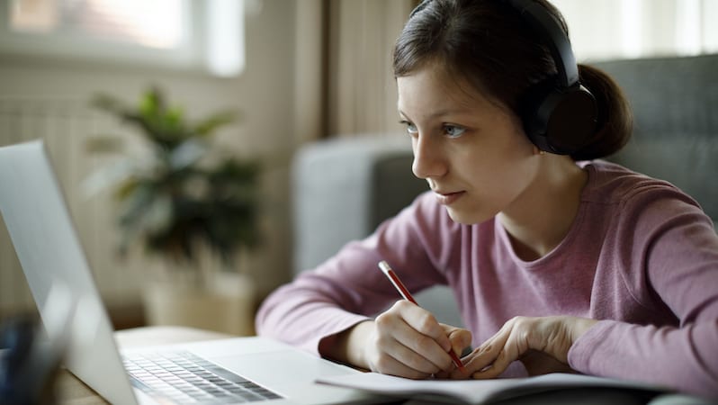 Adolescente estudiando en casa usando una laptop.