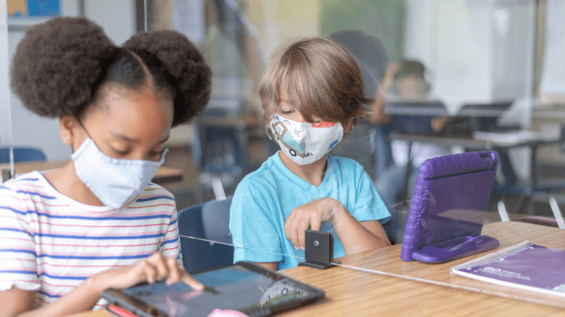 Dos estudiantes enmascarados trabajando en iPads