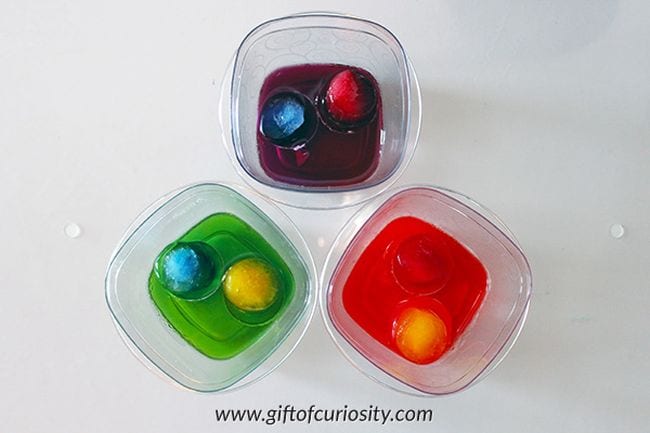 Recipiente de plástico con cubitos de hielo de colores flotando en agua de diferentes colores
